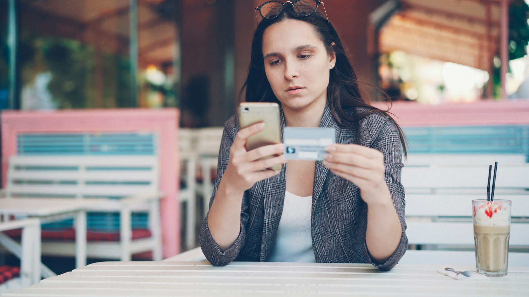 A woman at a café holding a bank card and her phone